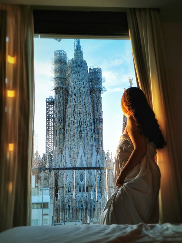 Claire in a hotel bedroom looking out the window at a view of the Sagrada Familia - the Sercotel Rossello