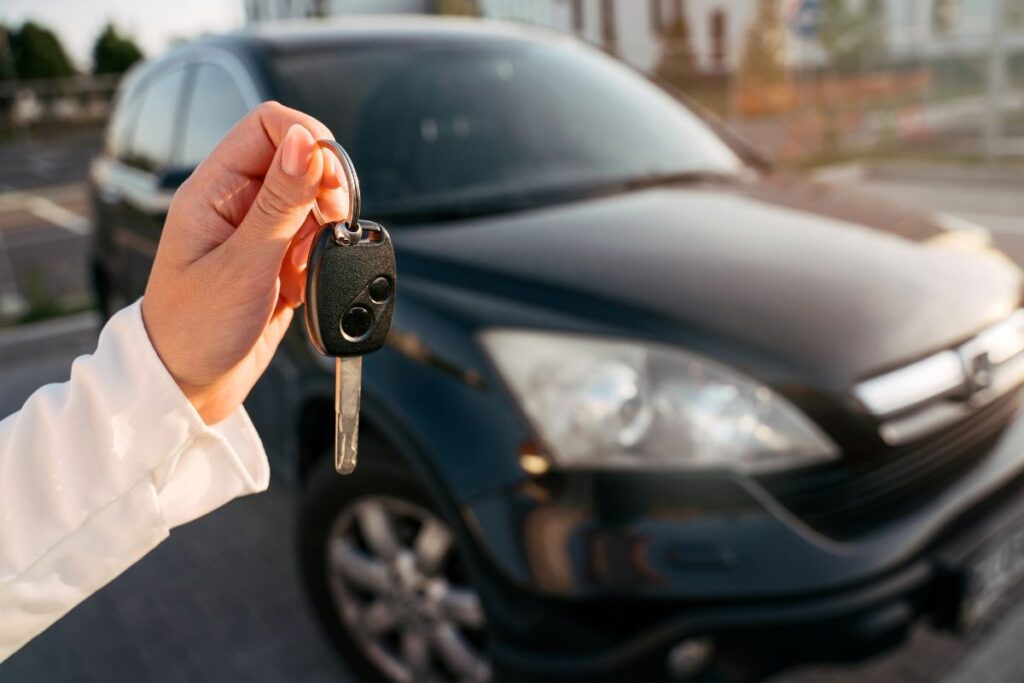 Womans hand holding a car key with a black car in the background - Car Rental in Barcelona